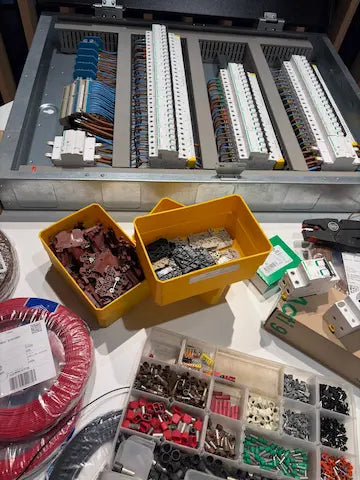 Blik in het atelier van Kompanjonn: een professioneel opgebouwd elektrisch verdeelbord met gestructureerd kabelbeheer, omringd door installatiematerialen zoals klemmen en automaten.